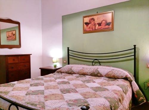 Camera Begonia al Podere Oca Bianca B&B a Pescia Romana con letto trapuntato rosa, pareti verdi e opere d'arte con cherubini
