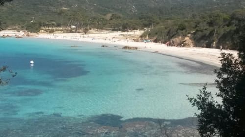 Petite crique méditerranéenne turquoise avec plage de sable blanc, bateau amarré et végétation luxuriante en Corse