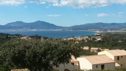 Villa méditerranéenne en Corse surplombant une baie turquoise avec montagnes, toits en terre cuite et oliviers