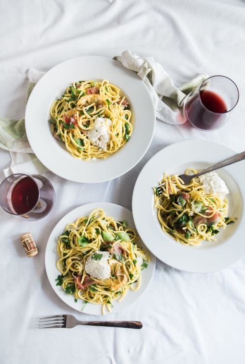 Three plates of spaghetti pasta with fresh vegetables, bacon, and cheese served with red wine at French Riviera House in