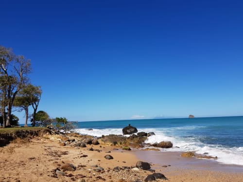 Plage tropicale pittoresque avec sable fin, rochers, vagues et végétation aux Gites villa Bagatelle à Sainte-Rose, Guadeloupe