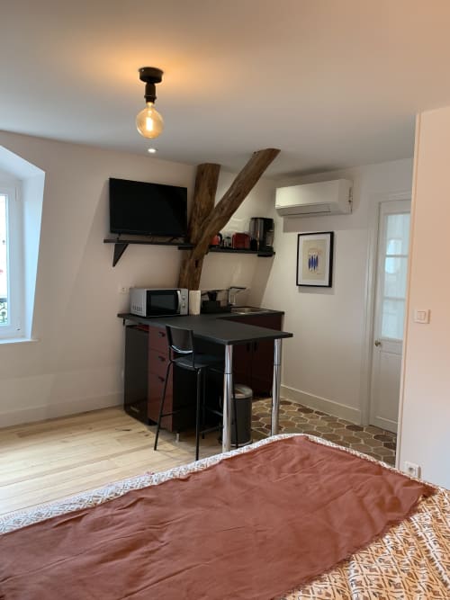 Modern studio apartment at Les Remparts De Joussaume with bed, work desk, TV, microwave, and wooden beam accent in