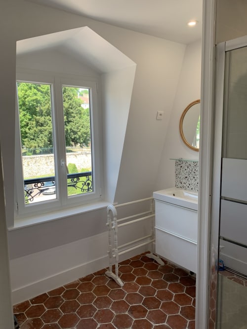 Modern bathroom with hexagonal terracotta tiles, white vanity, circular mirror, and French doors overlooking green landscape