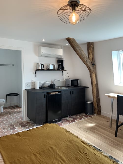 Studio apartment kitchenette with black cabinetry, rustic wooden beam, and garden view at Les Remparts de Joussaume,