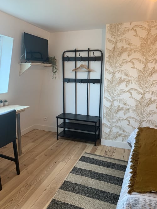 Modern bedroom at Les Remparts De Joussaume with black metal clothing rack, wooden floors, TV, and palm-print wallpaper in