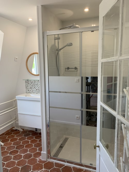 Modern bathroom with glass shower enclosure, white vanity, and terracotta hexagon floor tiles at Les Remparts De Joussaume