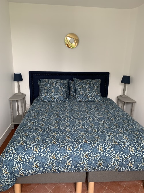 Bedroom with navy patterned bedding, black upholstered headboard, and gold wall sconce in Suite Le Héron at Les Remparts de