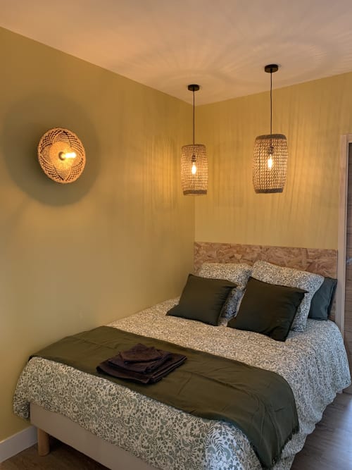 Cozy bedroom at Les Remparts De Joussaume with yellow walls, woven pendant lights, and patterned bedding in Château-Thierry