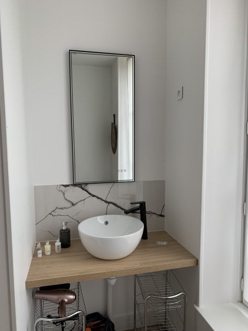Modern bathroom vanity with round white sink, black faucet, and lit mirror in Suite Le Renard et les raisins at Les Remparts