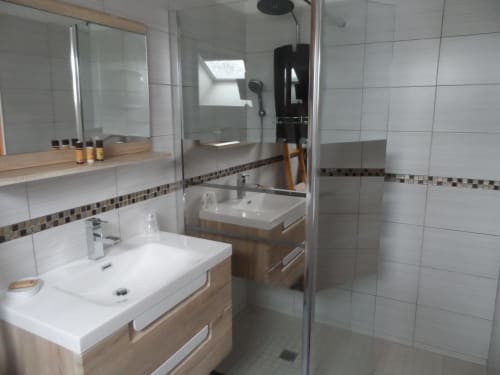 Salle de bains moderne avec vasques blanches, meuble en bois, douche vitrée et carrelage décoratif à CafecouetBreizh