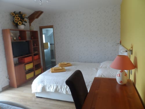 Chambre lumineuse avec lit blanc, mobilier en bois, TV, bureau et mur jaune à CafecouetBreizh B&B à Guipry-Messac