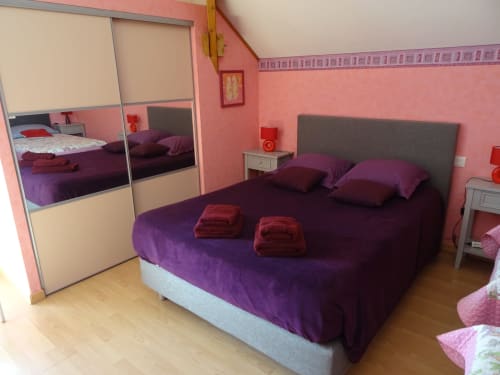 Chambre moderne de la CafecouetBreizh BnB avec literie violette, murs roses, armoire miroir et vue jardin à Guipry-Messac