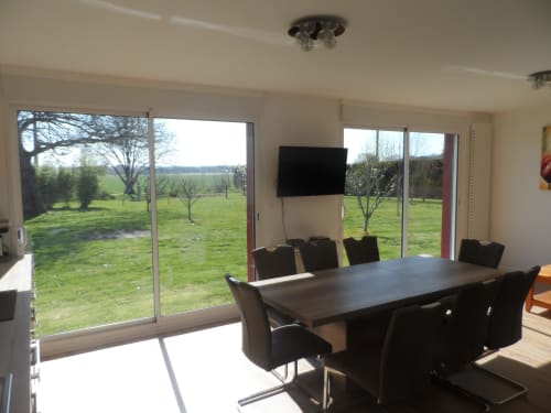 Salle à manger moderne avec table et chaises noires donnant sur un jardin verdoyant au gîte CafecouetBreizh à Guipry-Messac