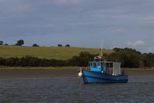 Bateau de pêche bleu amarré sur la rivière près du gîte Cafecouet Breizh à Guipry-Messac, France, avec collines verdoyantes