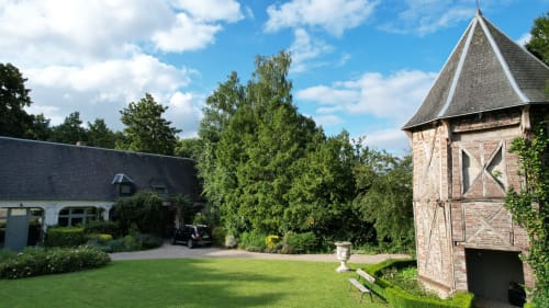 La cour de la Chambre d'Hôtes La Cour d'Hortense avec sa tour en pierre, sa pelouse impeccable et son architecture historique à Sailly-Flibeaucourt