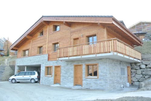 Chalet alpin moderne à La Tzoumaz avec base en pierre, étages supérieurs en bois, balcon et vue sur les montagnes