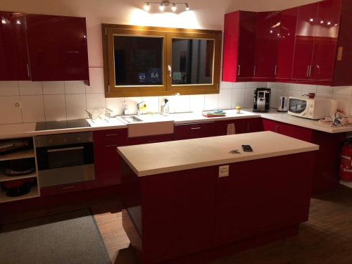 Cuisine moderne aux armoires rouges, comptoirs blancs et îlot central à l'auberge La Tzoumaz