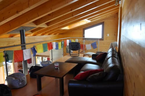 Espace commun lumineux en bois avec canapé noir en cuir, table à manger et drapeaux colorés à l'auberge La Tzoumaz
