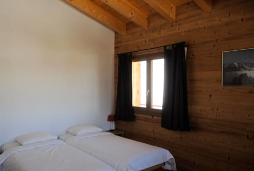 Chambre douillette à deux lits jumeaux à l'auberge La Tzoumaz, avec rideaux noirs et vue montagne par la fenêtre