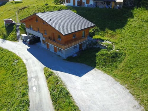 Vue aérienne du gîte La Tzoum'hostel à La Tzoumaz avec toit métallique, façade bois, piscine bleue et environnement montagneux