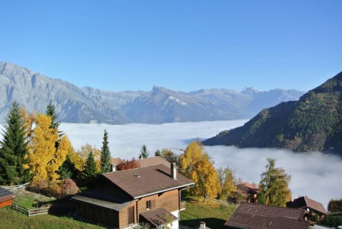 Le refuge de montagne La Tzoumaz surplombant une vallée alpine avec des pics brumeux et le feuillage automnal, Suisse.