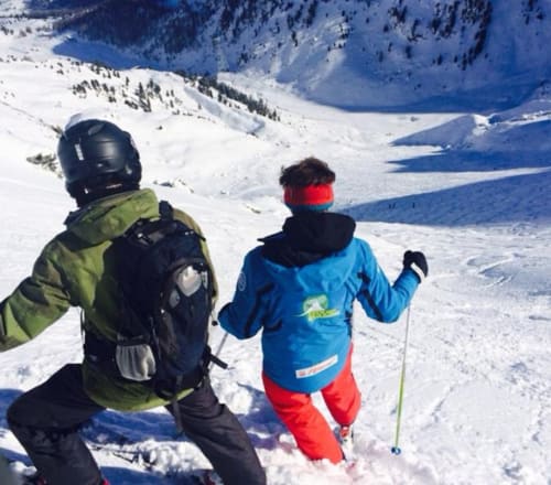 Deux skieurs profitent des pentes enneigées alpines près de La Tzoumaz avec des pics montagneux immaculés et un lac bleu en arrière-plan
