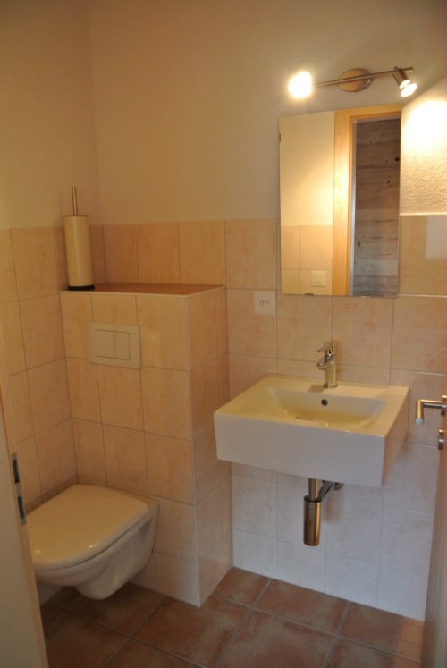 Salle de bain moderne avec toilettes murales, lavabo blanc et murs carrelés à l'auberge La Tzoumaz