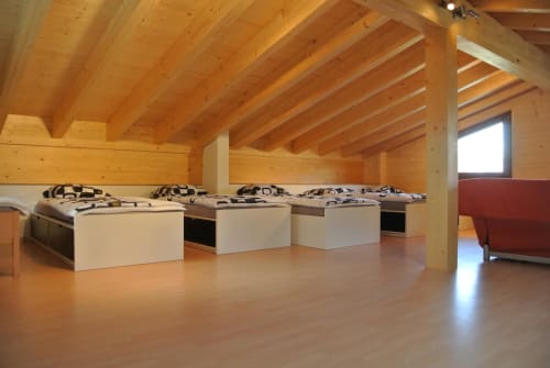 Chambre spacieuse sous les combles de La Tzoum'hostel avec plusieurs lits, poutres en bois et vue sur les montagnes de La Tzoumaz