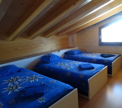 Chambre douillette en attique à La Tzoum'hostel avec trois lits décorés de flocons bleus et poutres en bois à La Tzoumaz