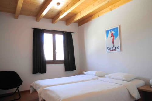 Chambre familiale à l'auberge La Tzoumaz avec deux lits, poutres en bois, affiche paysage montagnard et rideaux noirs