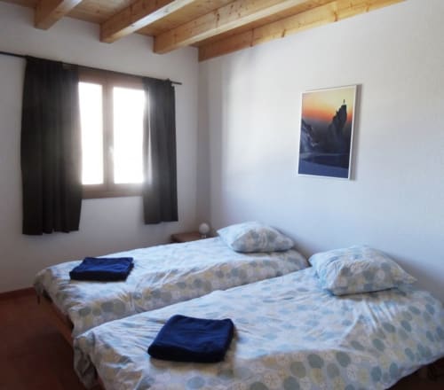 Chambre familiale avec deux lits à l'auberge La Tzoumaz, photographie de montagne au mur, poutres en bois, rideaux noirs