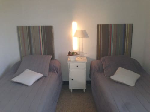 Twin beds with striped headboards and white pillows in a cottage bedroom with bedside lamp and nightstand at Gites Mas D'en