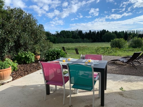 Outdoor dining area at Gites Mas D'en Ratéro cottage with colorful chairs, table set for breakfast, garden views and cypress