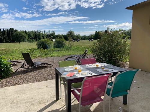Outdoor terrace at Gites Mas D'en Ratéro cottage in Thuir with dining table, colorful chairs, and countryside garden views