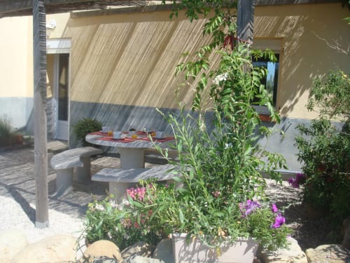 Outdoor patio with picnic table, flowering plants, and pergola shade at Gites Mas D'en Ratéro cottage in Thuir, France