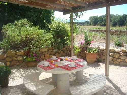 Shaded patio dining area at Gites Mas D'en Ratéro with stone table, red checkered tablecloths, and countryside mountain views