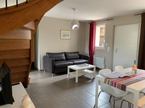 Modern cottage living area with black sofa, dining table, and wooden staircase at Gites Mas D'en Ratéro, Thuir