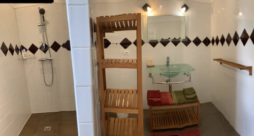 Modern bathroom in Thuir cottage with shower, green glass sink, wooden shelving, and black diamond tile accents