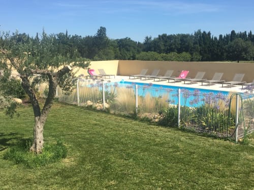 Fenced pool with lounge chairs at Gites Mas D'en Ratéro in Thuir, France, surrounded by gardens and trees