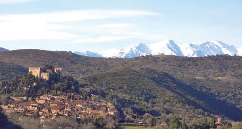 Château médiéval dominant le village aux toits en terre cuite de Thuir, France, avec les Pyrénées enneigées en arrière-plan
