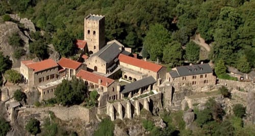 Château médiéval en pierre aux toits de tuiles rouges, niché dans les collines boisées de Thuir, France