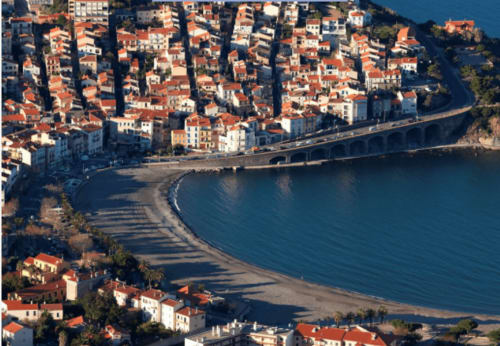 Vue aérienne d'une petite ville côtière méditerranéenne avec bâtisses aux toits rouges, plage et eaux bleues près de Thuir, France