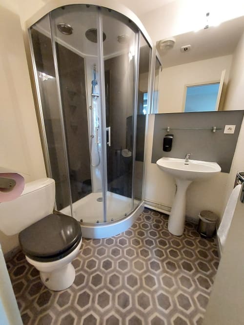 Salle de bains moderne au gîte Le Comtois Saône avec douche d'angle, lavabo blanc et carrelage géométrique