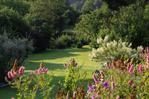 Jardin luxuriant de la maison d'hôtes La Bageatière avec fleurs roses, pelouse verte et arbres à Lépin-le-Lac