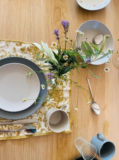 Elegant table setting at Maison Monsieur Léger with wildflowers, dinnerware, and gold-patterned napkin on wood