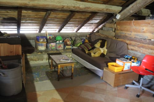Rustic attic space at La Maison De L'Épine B&B in Aime la Plagne with exposed beams, couch, storage, and wooden furnishings
