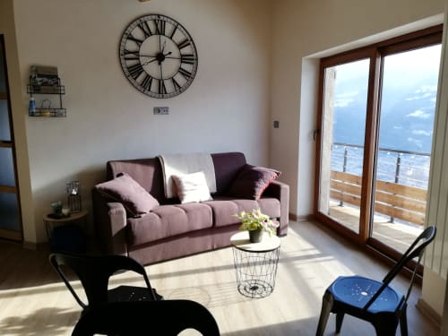 Bright living room with mauve sofa, Roman numeral clock, and mountain view from balcony at La Maison De L'Épine, Aime la