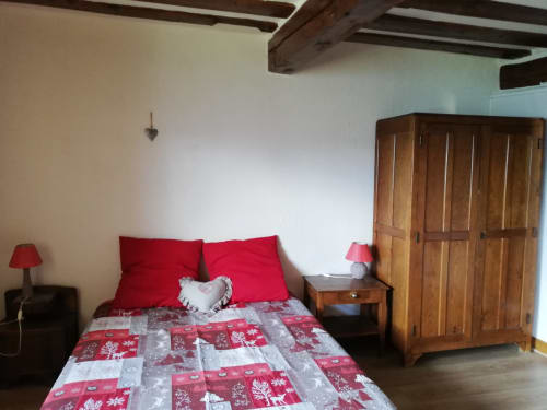 Cozy bedroom at La Maison De L'Épine cottage with red bedding, wooden wardrobe, and exposed beams in Aime la Plagne
