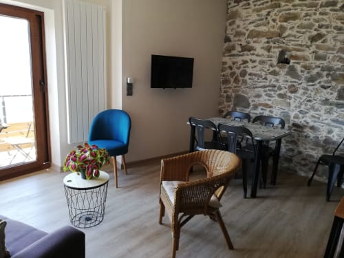 Modern cottage sitting area with blue chair, wicker furniture, stone wall, TV, and mountain views at La Maison De L'Épine