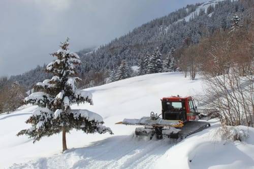 Red snow grooming vehicle clearing path at La Maison De L'Épine in snowy Aime la Plagne mountains